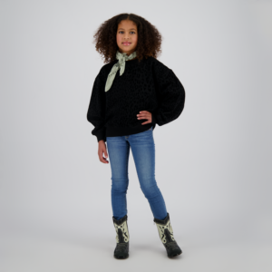 Young girl with curly hair wearing a black leopard-print sweatshirt, light scarf, blue jeans, and cowboy boots, standing with hand on hip.
