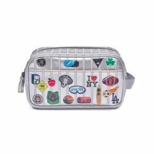 Silver mini crossbody bag covered in colorful travel patches and pins, front view with zipper closure and strap edge visible.