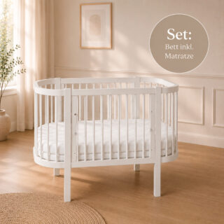 Round white baby crib with a mattress in a bright, neutral nursery; a 'set with mattress included' label appears in the corner (German text).