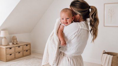 Mother cuddling a smiling baby in a light, cozy nursery with a wooden dresser and woven baskets nearby