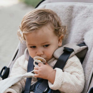 Baby sitting in a stroller wearing a cream knit sweater, sucking a pacifier.