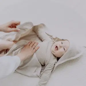 Baby lying on a soft blanket while an adult places a cloth diaper around them during a diaper change.