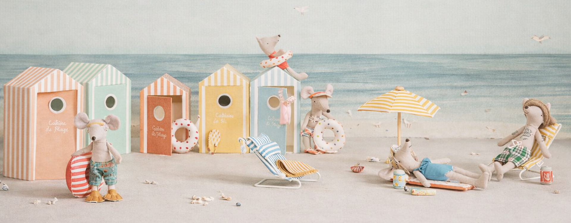 Pastel-striped beach huts at the shore with plush mice in swimsuits relaxing by the sea.