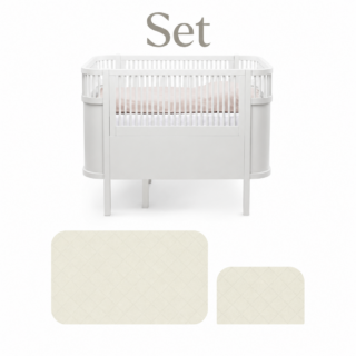White baby crib with slatted rails and two beige quilted pads lying below the set text