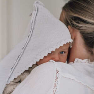 Newborn baby peeking from under a white lace bonnet, resting on an adult's shoulder.