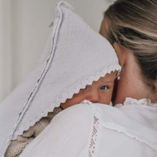 Newborn baby peeking from under a white lace bonnet, resting on an adult's shoulder.
