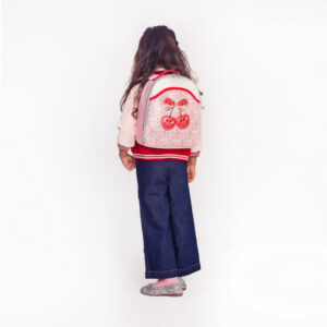 Back view of a young girl wearing a pink jacket and wide-leg jeans, with a floral backpack featuring two cherries, standing against a white background.
