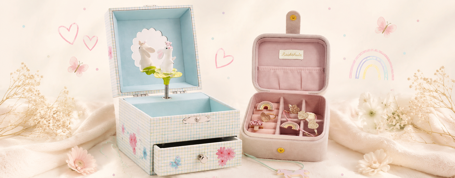 Pastel jewelry boxes: a blue plaid lift-top box with a bunny figurine inside, and a pink velvet case with ring compartments, set on a soft pink background.
