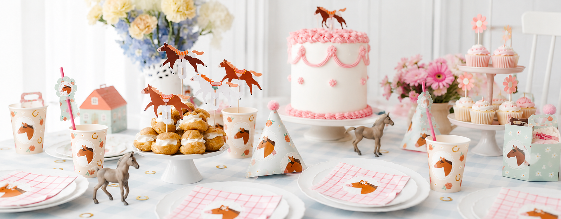 Pastel horse-themed birthday table with a pink-iced cake, cupcakes, party hats, and horse décor.