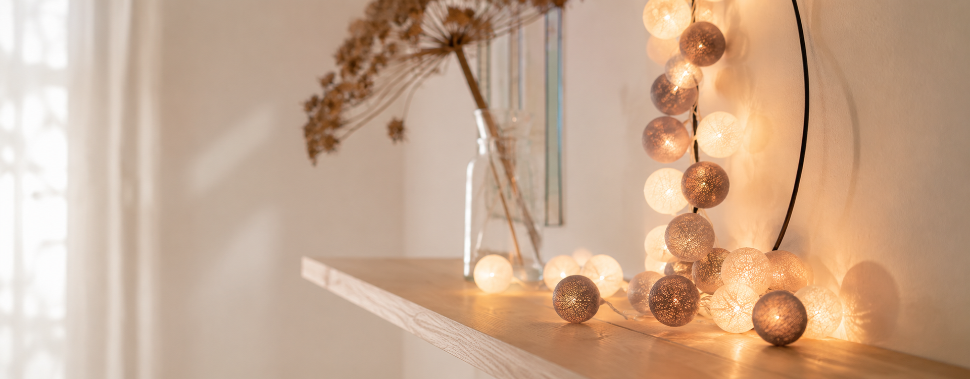 Cozy decorative string lights glow warm on a wooden shelf beside a glass vase with dried flowers.