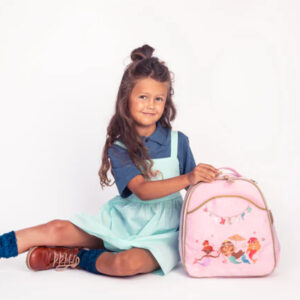 Young girl sitting on the floor with a pink backpack featuring princess graphics and a teal dress beneath a blue shirt.