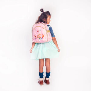 Young girl with a pink princess backpack, wearing a blue top and mint dress, facing away in a playful pose.