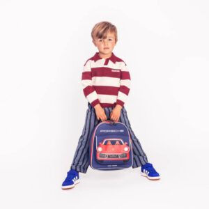 Young boy in a maroon-and-white striped sweater holds a blue Porsche backpack with a red car graphic in a white studio.