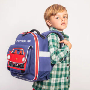 Young child with a blue backpack featuring a red Porsche car design on the front, wearing a green plaid shirt.