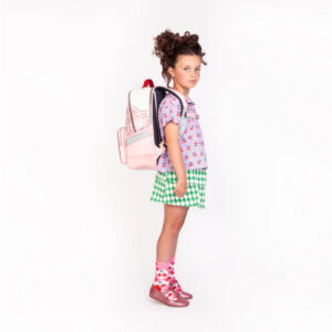 Young girl in profile wearing a pink backpack, purple patterned shirt, green diamond skirt, pink socks, and pink shoes.