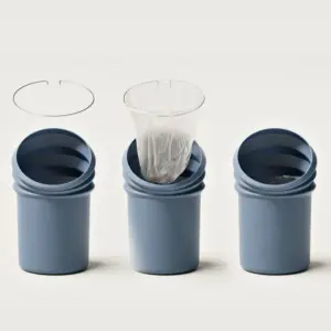 Three blue cylindrical waste bins in a row with a plastic bag being placed into the middle bin.