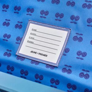 White registration form with lines for Name, School, Phone and Address placed on blue fabric patterned with small cherry motifs; bottom text reads 'JEUNE PREMIER'.