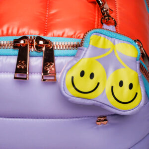 Close-up of a purple bag with gold zippers and a yellow smiley-face cloud keychain.