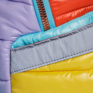 Close-up of a multicolor puffer jacket with a blue zipper, showing purple, teal, red, gray, and yellow quilted panels.