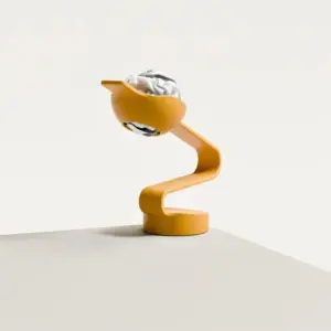 Orange spiral desk sculpture balancing a crumpled paper ball in a bowl on a pale surface.