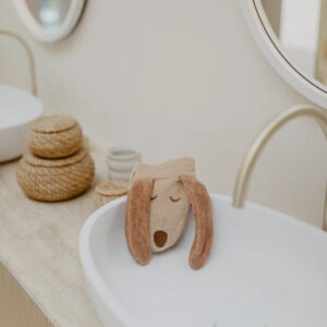 Beige plush dog with long ears rests on the edge of a white bathroom sink.
