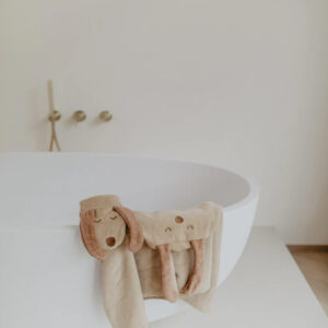 White freestanding bathtub with two beige plush dog-shaped towels draped over the edge, one with floppy ears and a smiling face.