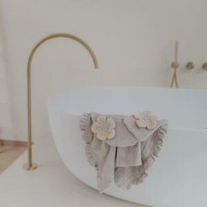 White freestanding bathtub with a gray towel featuring fabric flowers draped over the edge and a gold faucet in the background.
