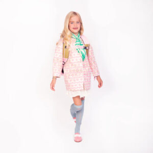 Girl in a pink patterned coat with a mint scarf and backpack, standing against a white background in a studio.