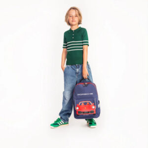 Boy standing in a green striped polo, jeans, green sneakers, holding a blue Porsche backpack with a red car graphic