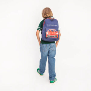 Child with back to camera wearing a green shirt and jeans, carrying a purple backpack decorated with a red Porsche sports car.