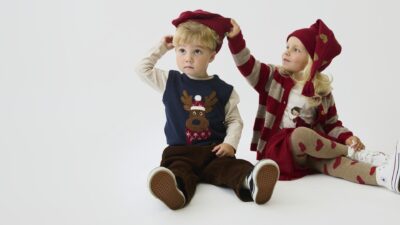Zwei Kinder in Weihnachtsmode von Hust & Claire: Rentierweste, gestreifte Strickjacke, Mützen und Herz-Strumpfhose